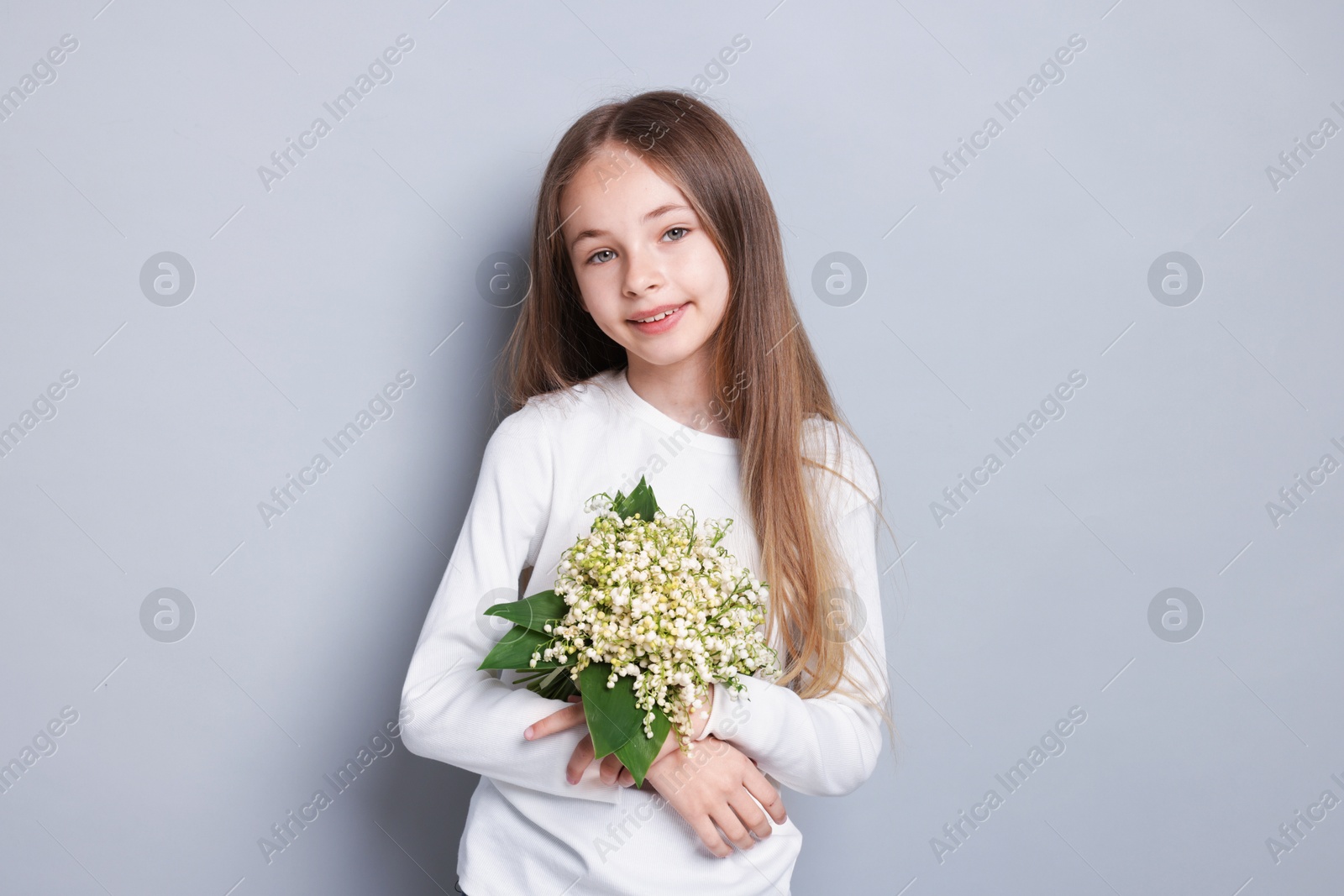 Girl with bouquet of beautiful lily-of-the-valley flowers on light grey background Photo of Girl with bouquet of beautiful lily-of-the-valley flowers on light grey background