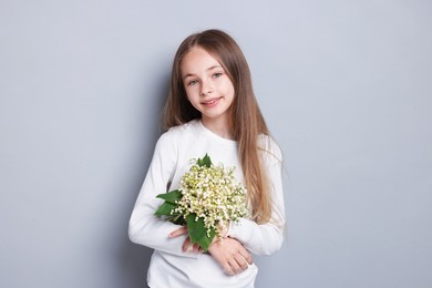 Photo of Girl with bouquet of beautiful lily-of-the-valley flowers on light grey background