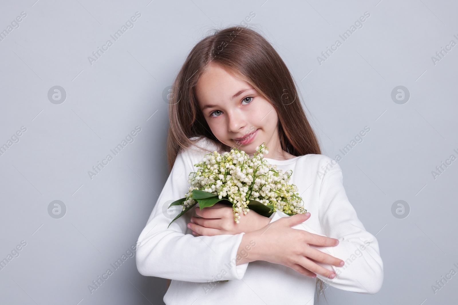 Girl with bouquet of beautiful lily-of-the-valley flowers on light grey background Photo of Girl with bouquet of beautiful lily-of-the-valley flowers on light grey background
