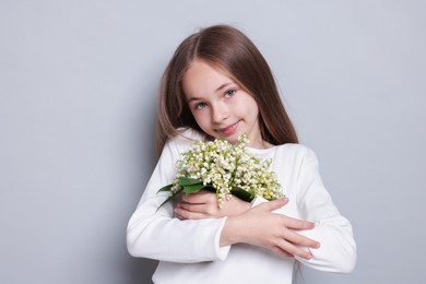 Photo of Girl with bouquet of beautiful lily-of-the-valley flowers on light grey background