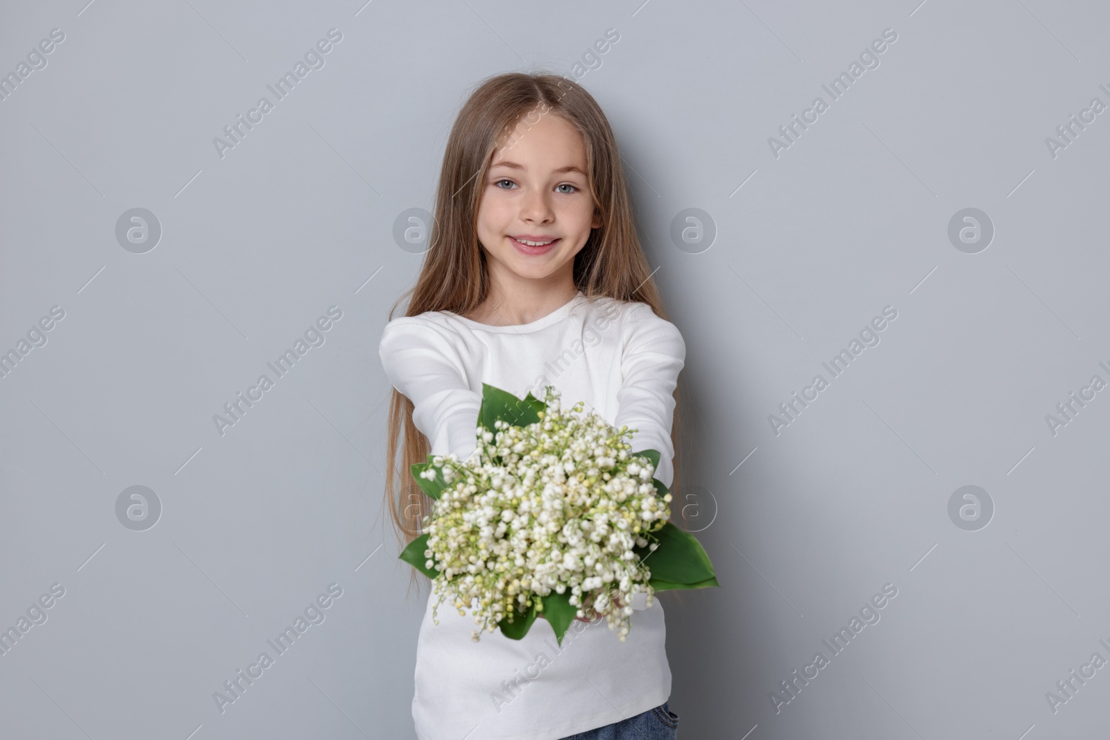 Girl with bouquet of beautiful lily-of-the-valley flowers on light grey background Photo of Girl with bouquet of beautiful lily-of-the-valley flowers on light grey background