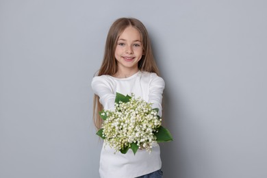 Photo of Girl with bouquet of beautiful lily-of-the-valley flowers on light grey background