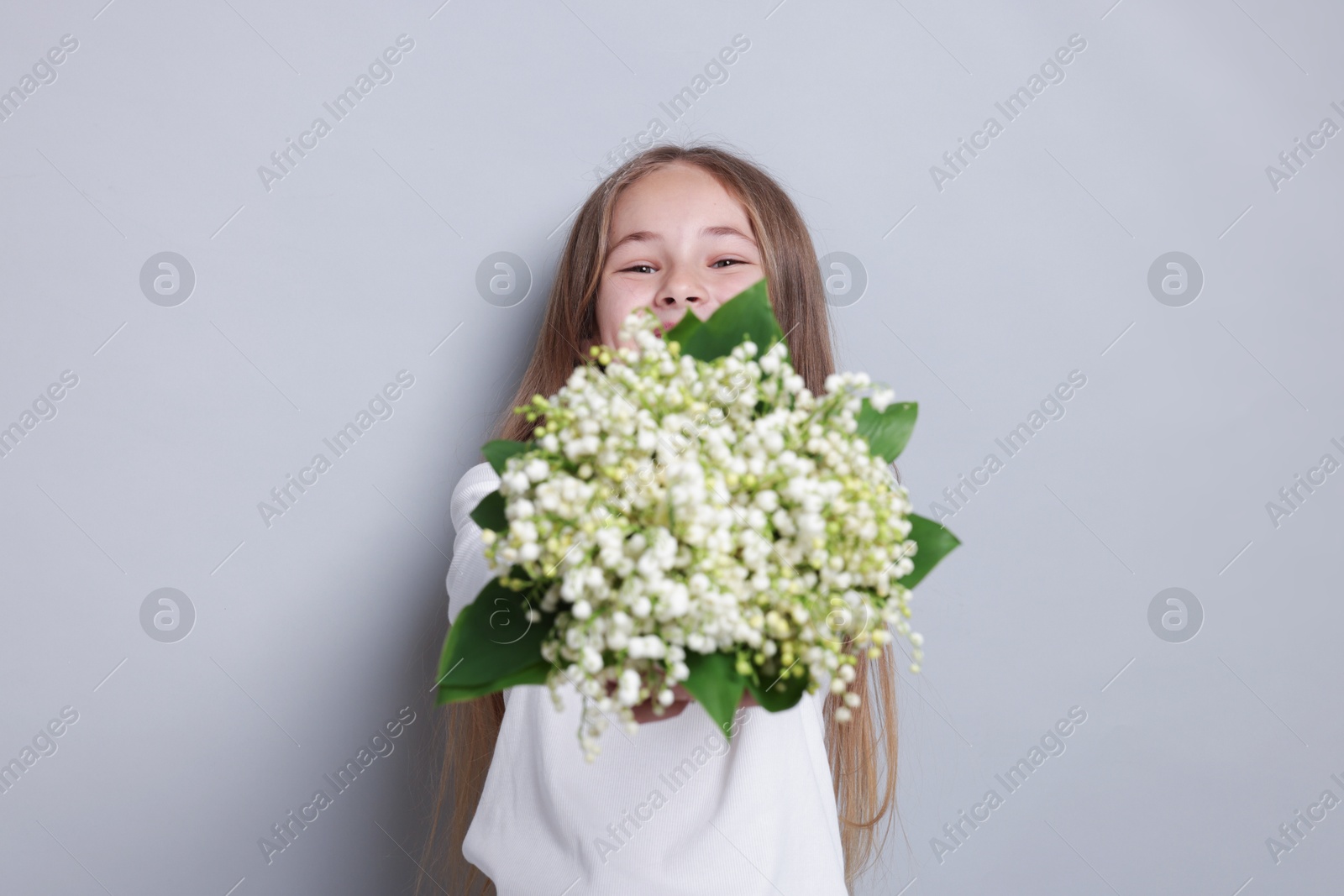 Girl with bouquet of beautiful lily-of-the-valley flowers on light grey background Photo of Girl with bouquet of beautiful lily-of-the-valley flowers on light grey background