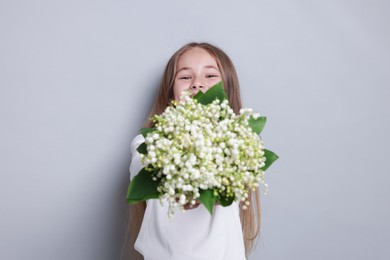 Photo of Girl with bouquet of beautiful lily-of-the-valley flowers on light grey background