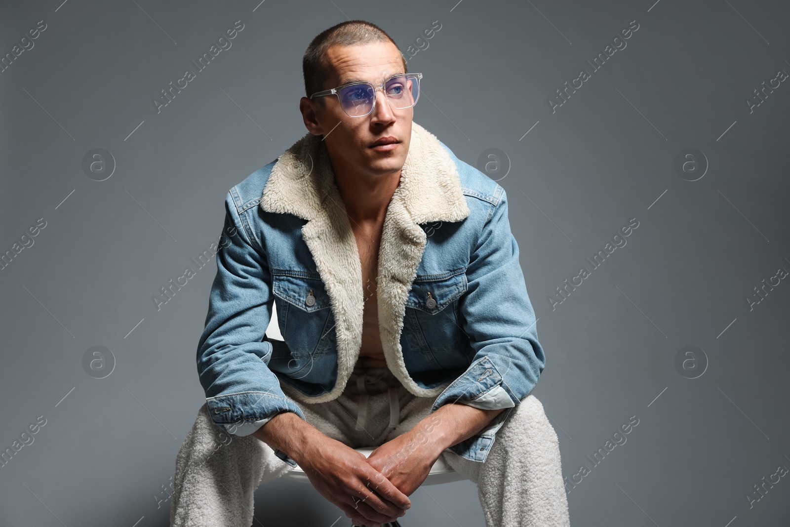 Fashionable portrait of handsome man in stylish outfit on chair against grey background Photo of Fashionable portrait of handsome man in stylish outfit on chair against grey background