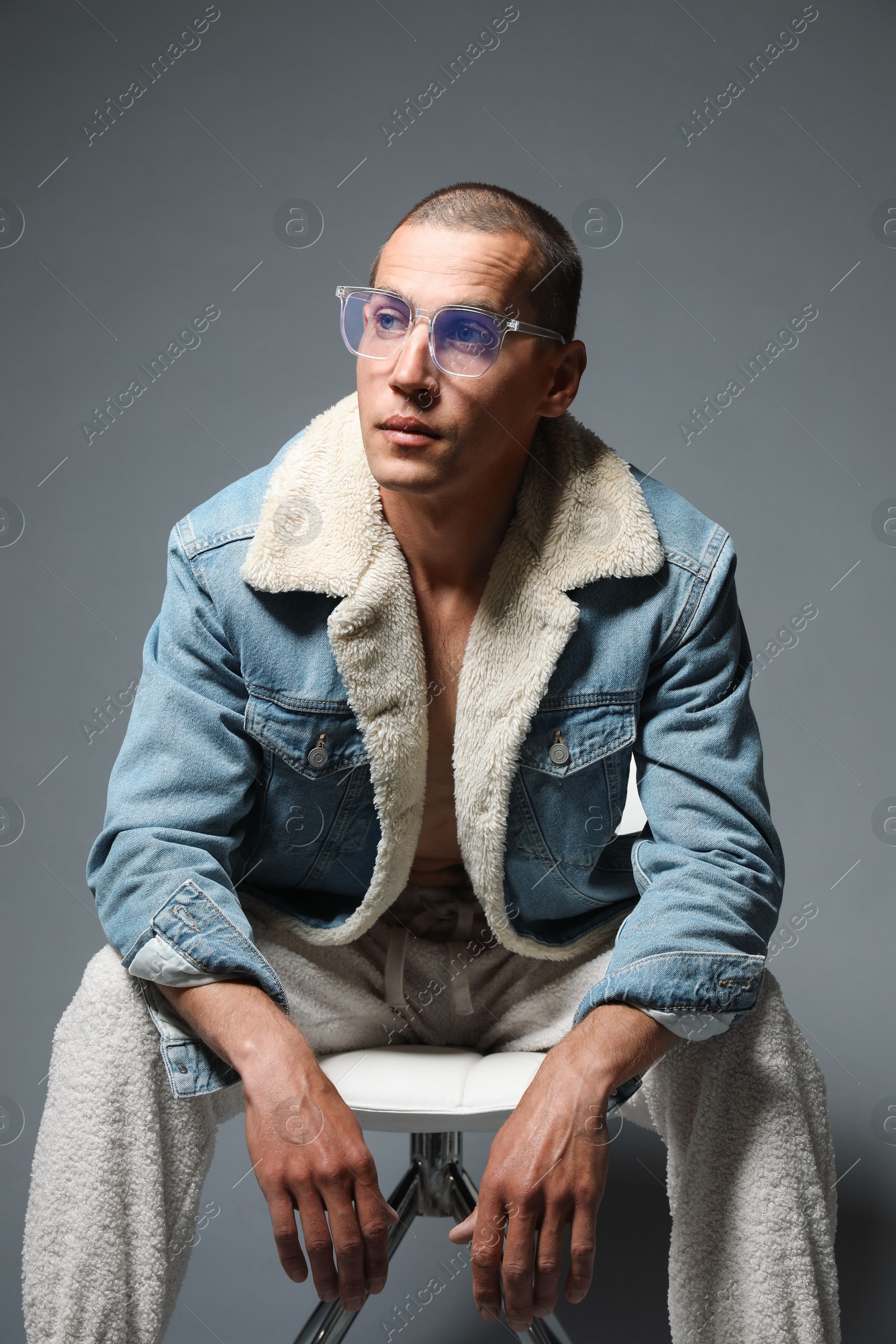 Fashionable portrait of handsome man in stylish outfit on chair against grey background Photo of Fashionable portrait of handsome man in stylish outfit on chair against grey background