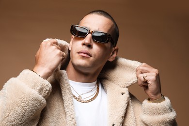 Photo of Fashionable portrait of handsome man in stylish outfit on brown background