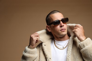 Photo of Fashionable portrait of handsome man in stylish outfit on brown background, space for text