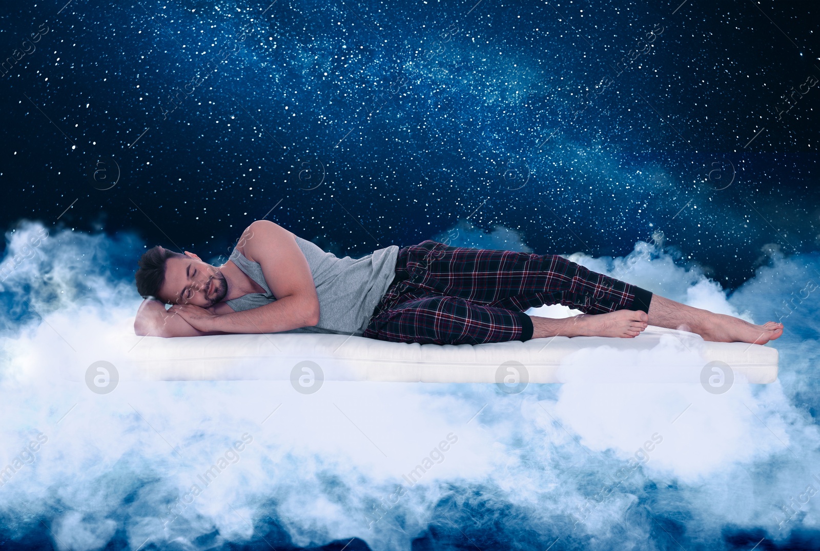 Young man sleeping on comfortable mattress as soft as cloud in starry sky at night Image of Young man sleeping on comfortable mattress as soft as cloud in starry sky at night