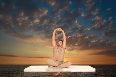 Image of Young man on comfortable mattress in sea at sunset