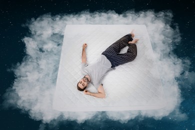 Image of Young man sleeping on comfortable mattress as soft as cloud in starry sky at night, above view