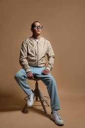 Photo of Fashionable portrait of handsome man in stylish outfit on brown background