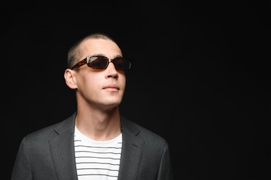 Photo of Fashionable portrait of handsome man in stylish outfit on black background, space for text
