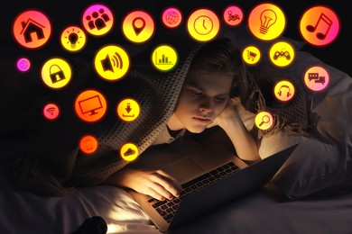 Image of Internet addicted teenager using laptop under blanket on bed at night. Different icons near him