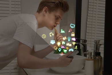 Image of Internet addicted teenager using mobile phone while brushing teeth in bathroom. Different icons flying out of device