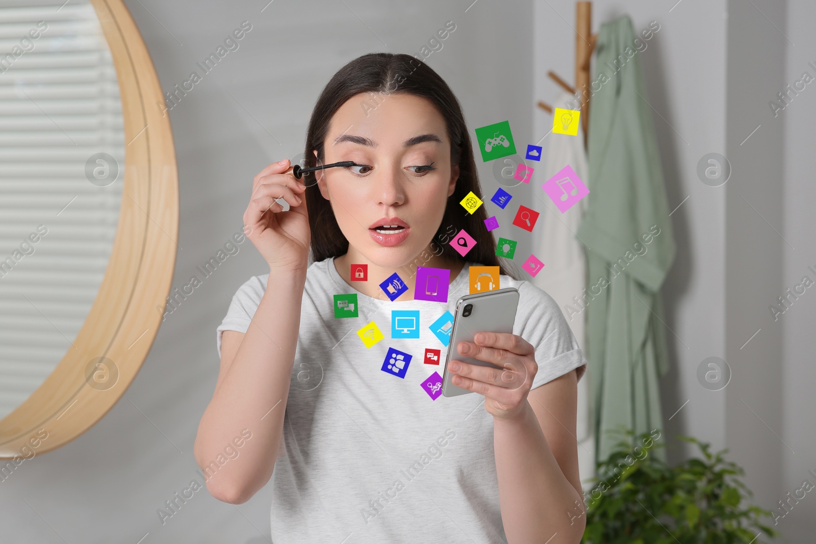 Internet addicted woman using mobile phone while applying mascara at home. Different icons flying out of device Image of Internet addicted woman using mobile phone while applying mascara at home. Different icons flying out of device
