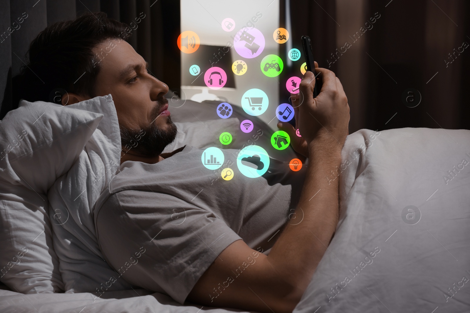 Internet addicted man using mobile phone instead of sleeping at night. Different icons flying out of device Image of Internet addicted man using mobile phone instead of sleeping at night. Different icons flying out of device