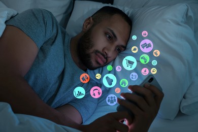 Image of Internet addicted man using mobile phone instead of sleeping at night. Different icons flying out of device