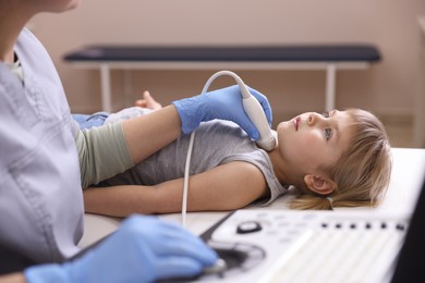 Photo of Sonographer conducting ultrasound examination of little girl's thyroid gland in clinic, closeup
