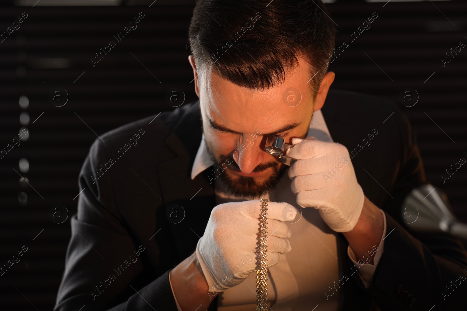 Appraiser with loupe evaluating luxury jewelry indoors Photo of Appraiser with loupe evaluating luxury jewelry indoors