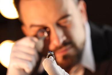 Photo of Appraiser with loupe evaluating luxury ring indoors, selective focus