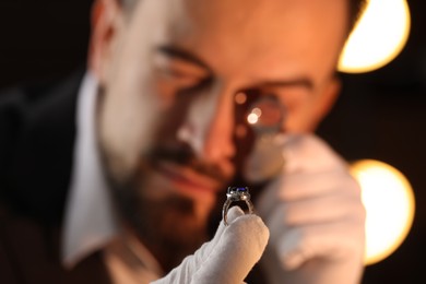 Photo of Appraiser with loupe evaluating luxury ring indoors, selective focus