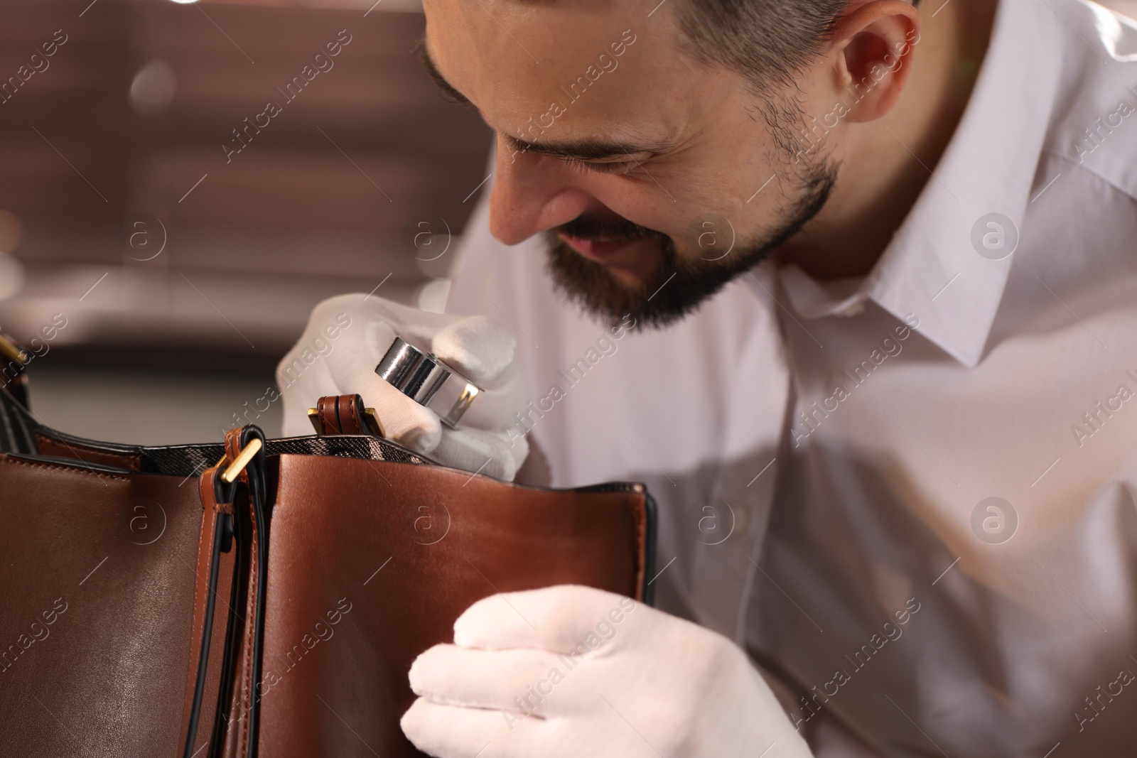 Appraiser with loupe evaluating leather bag indoors Photo of Appraiser with loupe evaluating leather bag indoors