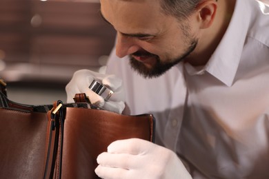 Photo of Appraiser with loupe evaluating leather bag indoors