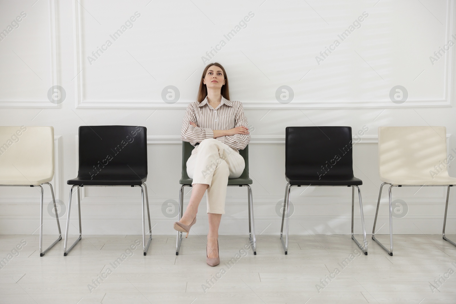 Woman sitting on chair and waiting for appointment indoors Photo of Woman sitting on chair and waiting for appointment indoors