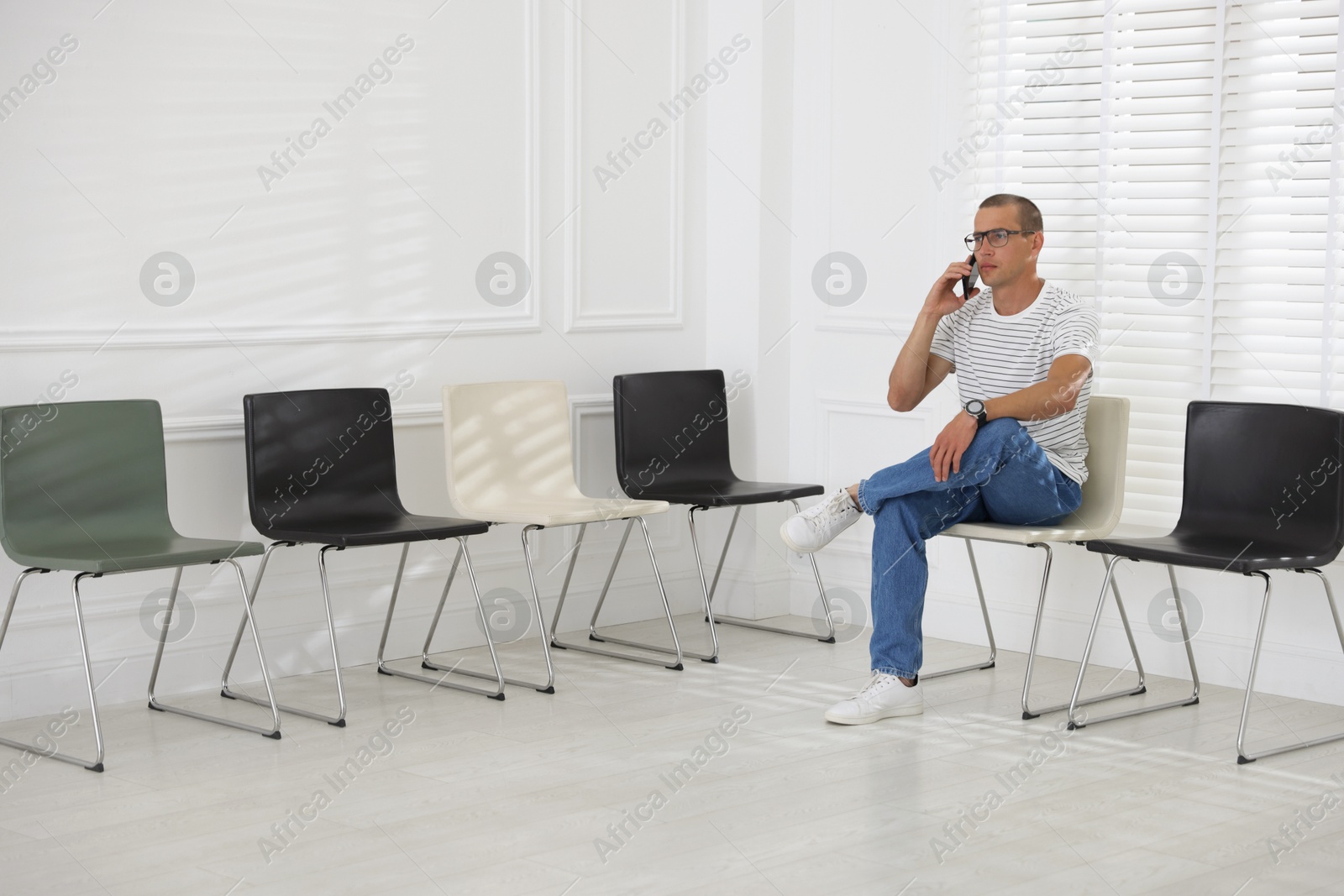 Man talking on smartphone while waiting for appointment indoors Photo of Man talking on smartphone while waiting for appointment indoors