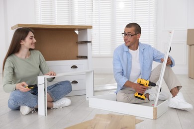 Photo of Happy couple assembling furniture on floor at home