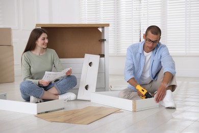Photo of Happy couple assembling furniture on floor at home