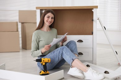 Photo of Smiling woman with manual assembling furniture on floor at home