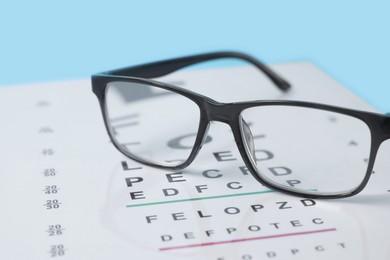 Photo of Glasses and vision test chart on light blue background, closeup