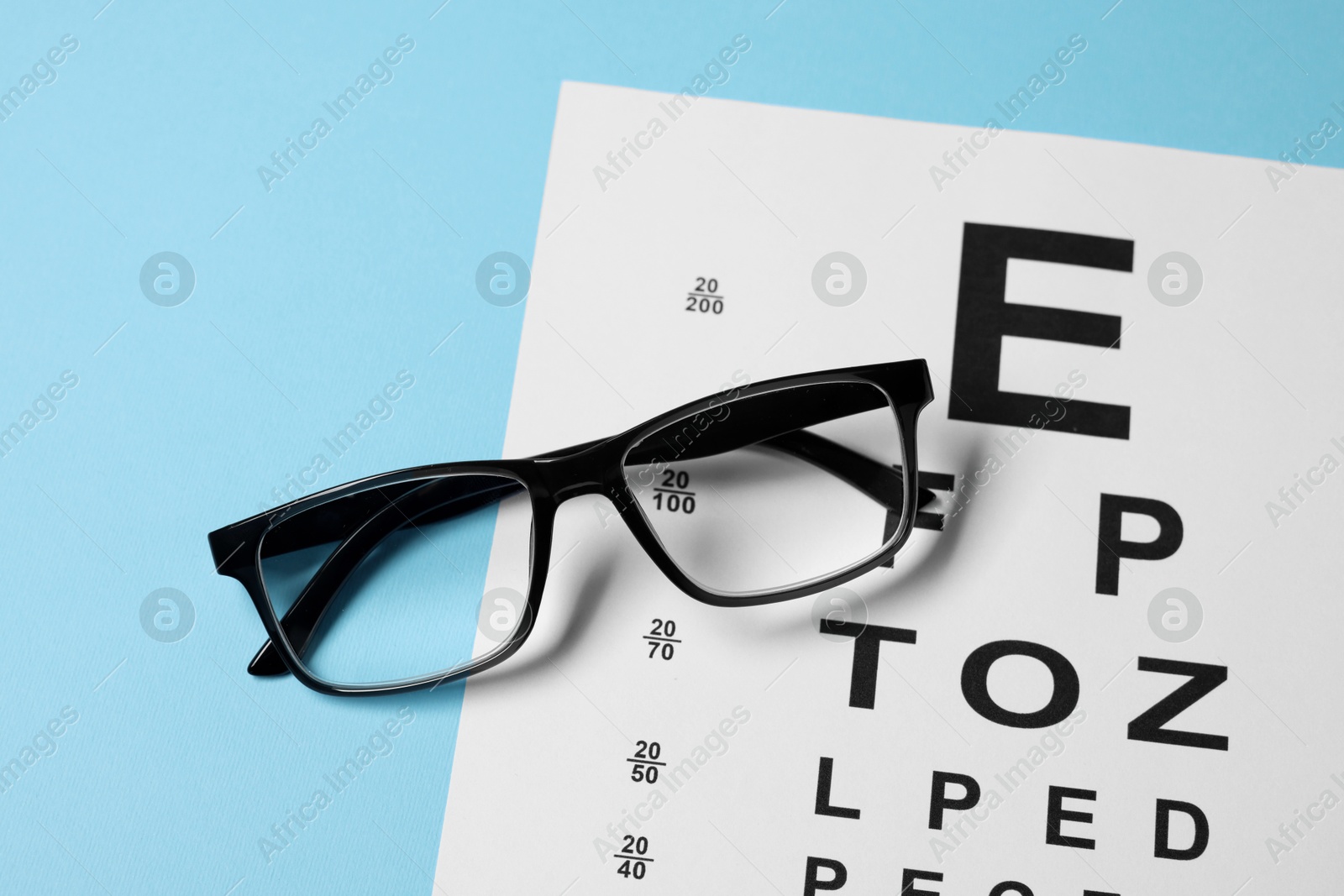 Glasses and vision test chart on light blue background, closeup Photo of Glasses and vision test chart on light blue background, closeup