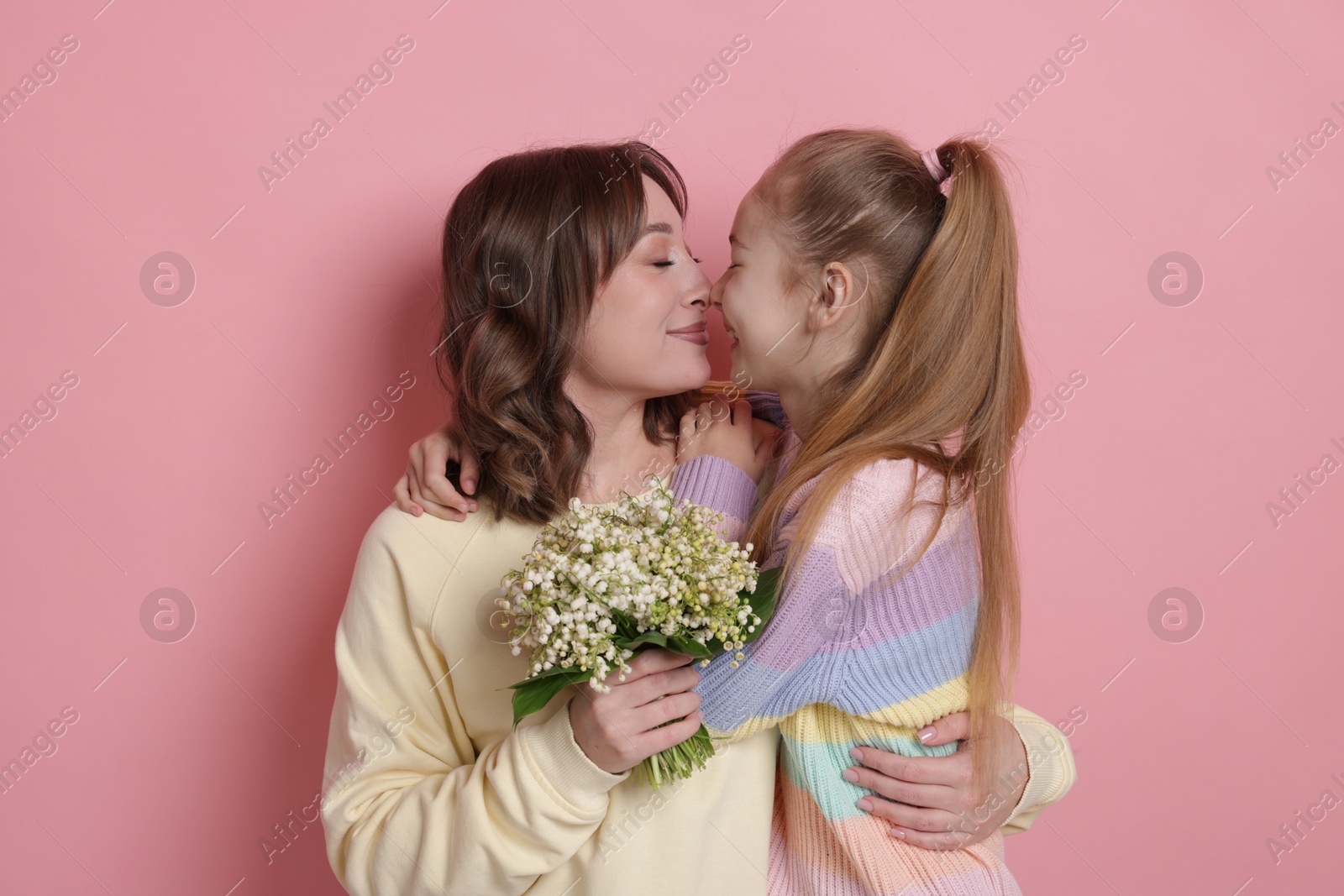 Girl giving her mother beautiful bouquet of lily-of-the-valley flowers on light pink background Photo of Girl giving her mother beautiful bouquet of lily-of-the-valley flowers on light pink background