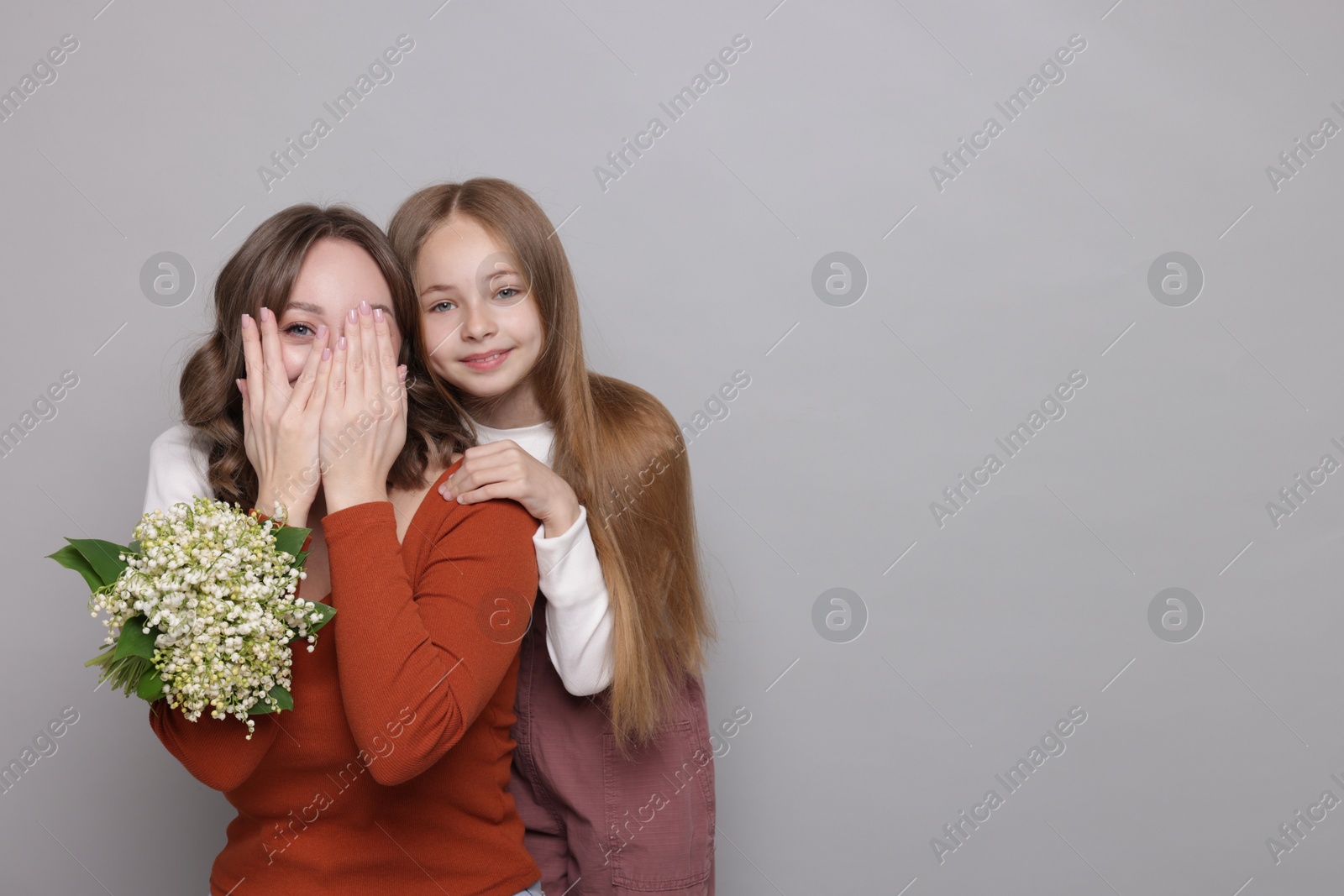 Girl giving her mom beautiful bouquet of lily-of-the-valley flowers on light grey background. Space for text Photo of Girl giving her mom beautiful bouquet of lily-of-the-valley flowers on light grey background. Space for text