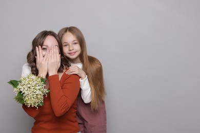 Photo of Girl giving her mom beautiful bouquet of lily-of-the-valley flowers on light grey background. Space for text