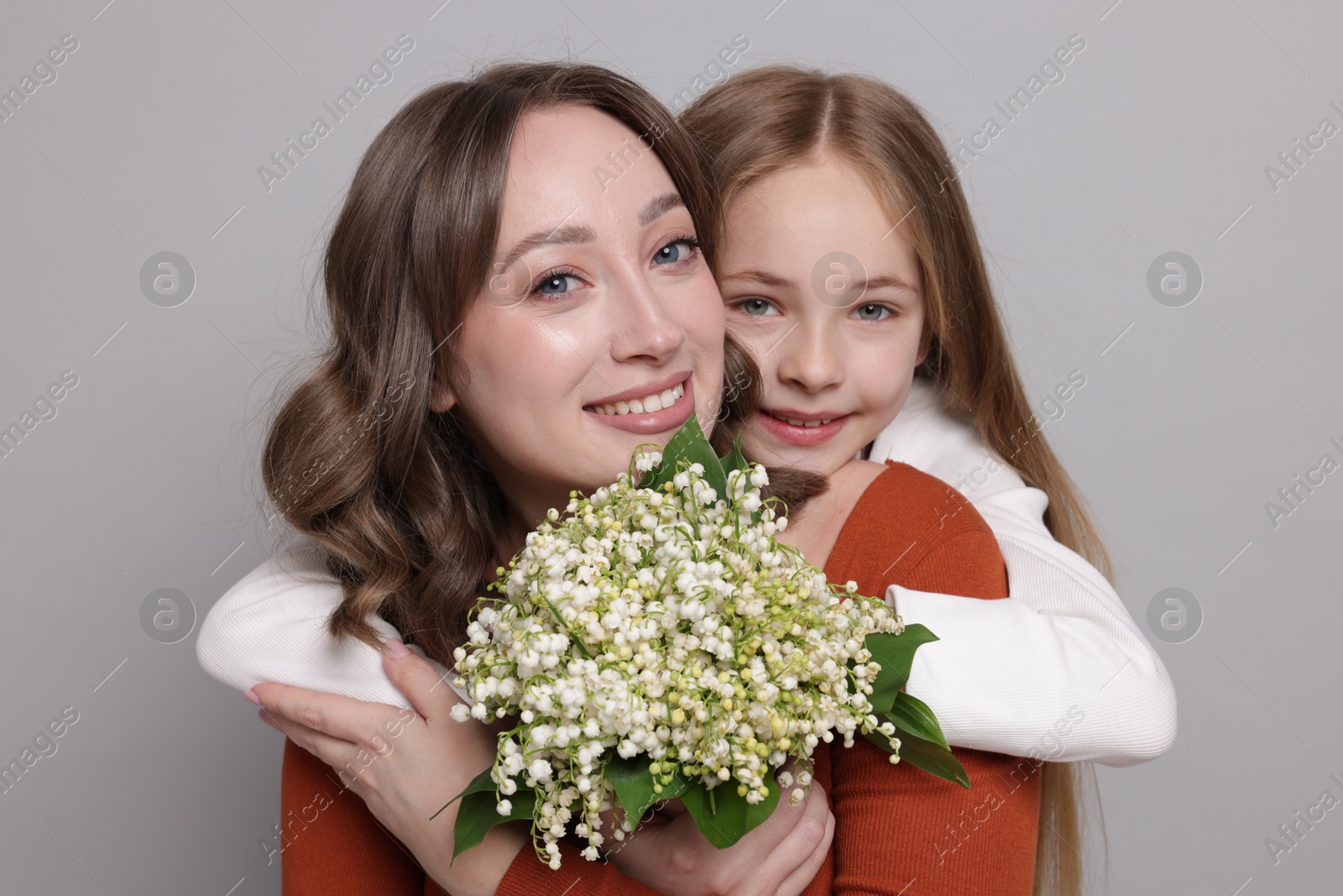 Girl giving her mom beautiful bouquet of lily-of-the-valley flowers on light grey background Photo of Girl giving her mom beautiful bouquet of lily-of-the-valley flowers on light grey background