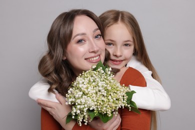 Photo of Girl giving her mom beautiful bouquet of lily-of-the-valley flowers on light grey background