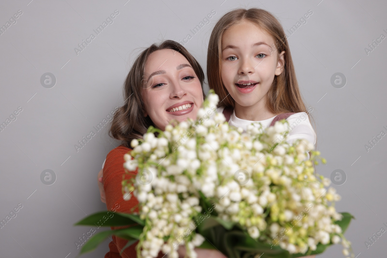 Girl giving her mom beautiful bouquet of lily-of-the-valley flowers on light grey background Photo of Girl giving her mom beautiful bouquet of lily-of-the-valley flowers on light grey background