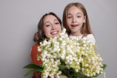 Photo of Girl giving her mom beautiful bouquet of lily-of-the-valley flowers on light grey background