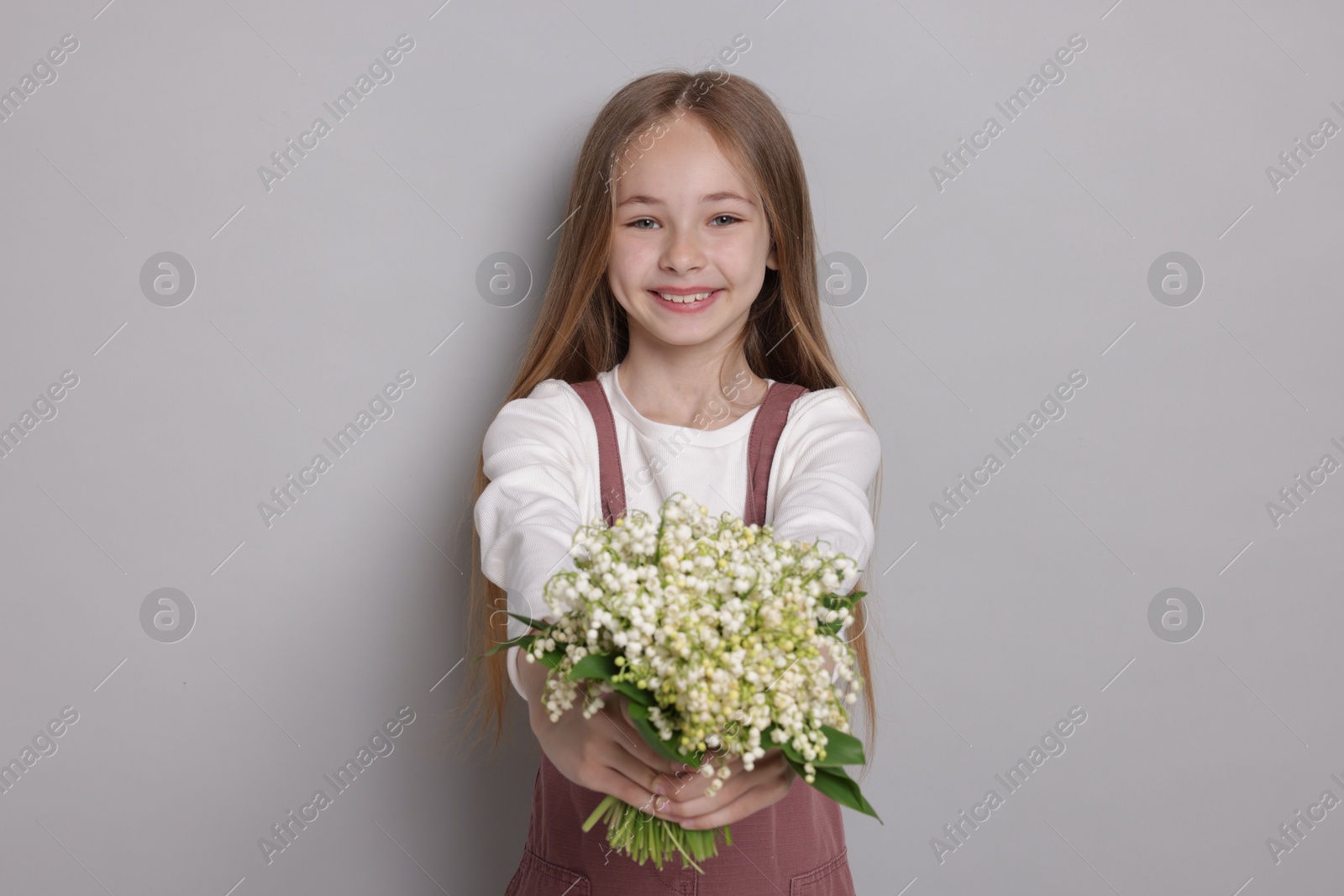 Girl with bouquet of beautiful lily-of-the-valley flowers on light grey background Photo of Girl with bouquet of beautiful lily-of-the-valley flowers on light grey background