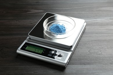 Photo of Laboratory scale with Petri dish of sample on wooden table, closeup