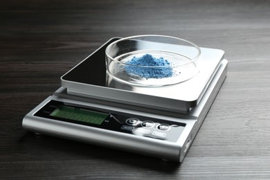 Photo of Laboratory scale with Petri dish of sample on wooden table, closeup