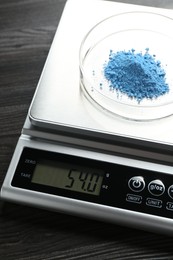 Photo of Laboratory scale with Petri dish of sample on wooden table, closeup