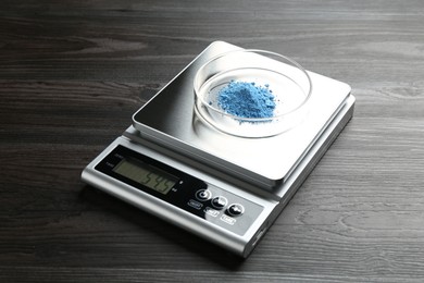 Photo of Laboratory scale with Petri dish of sample on wooden table, closeup