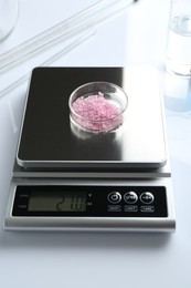 Photo of Scale with Petri dish of sample and other laboratory equipment on white background, closeup