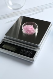 Photo of Scale with Petri dish of sample and other laboratory equipment on white background, closeup