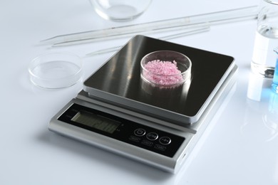 Photo of Scale with Petri dish of sample and other laboratory equipment on white background, closeup